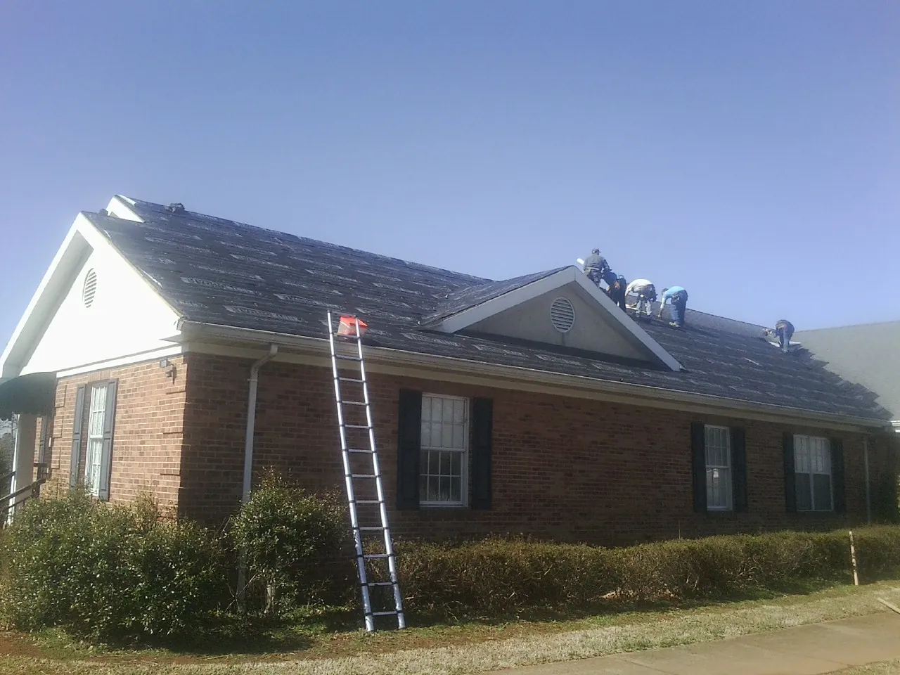 Crew tearing shingles off a brick ranch roof with a ladder set — Metal Roof Repair work by our crew in Apollo Beach