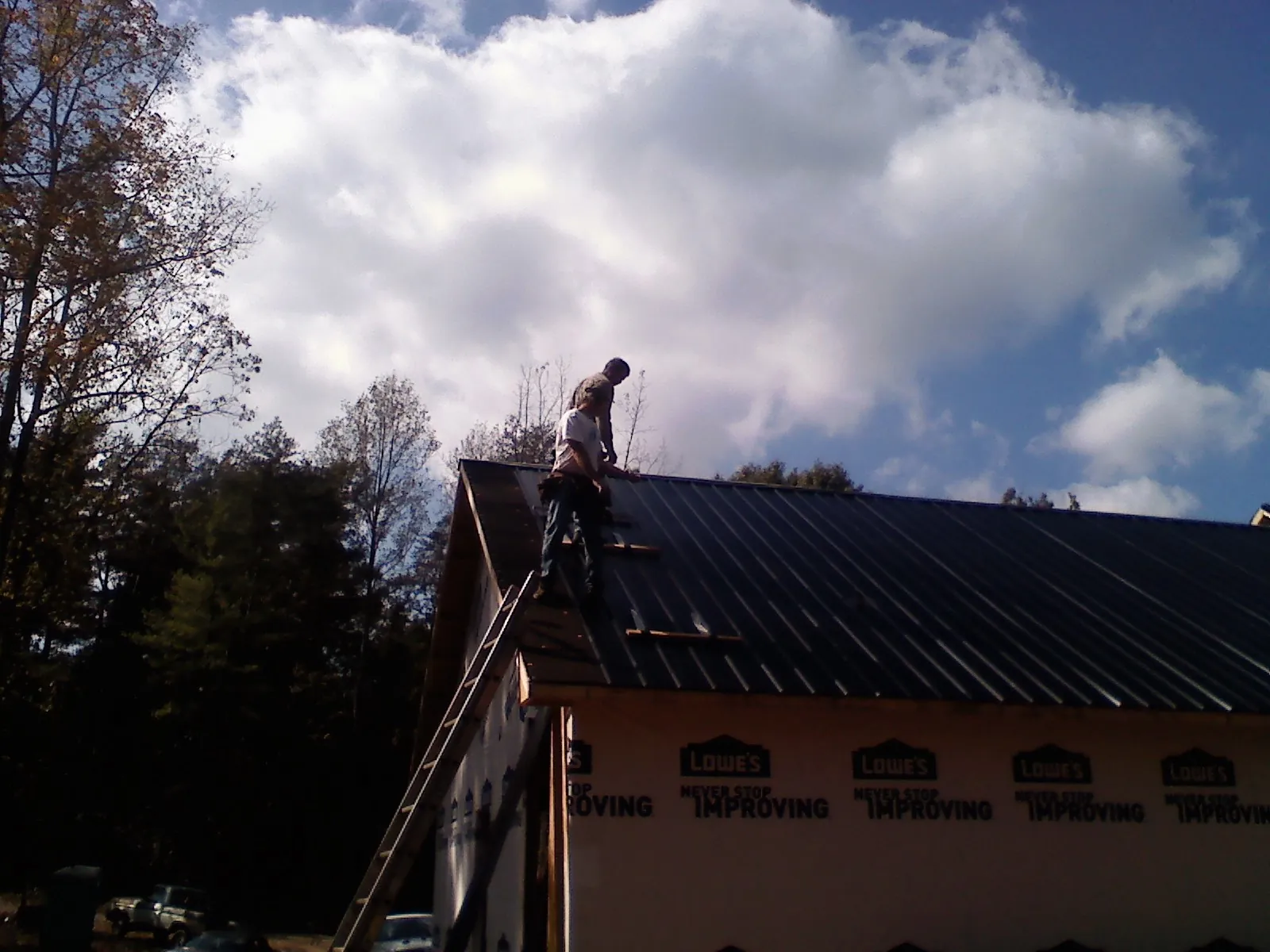 Roofer fastening dark metal panels high against a cloudy sky, from a Roof Inspection job in Apollo Beach