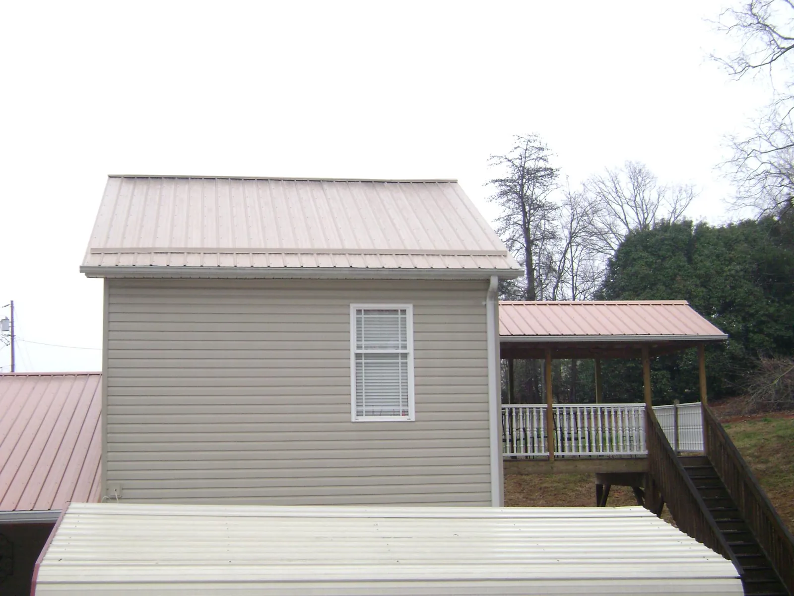 Tan metal roofs on a two story addition and attached porch, from a Roof Replacement job in Apollo Beach
